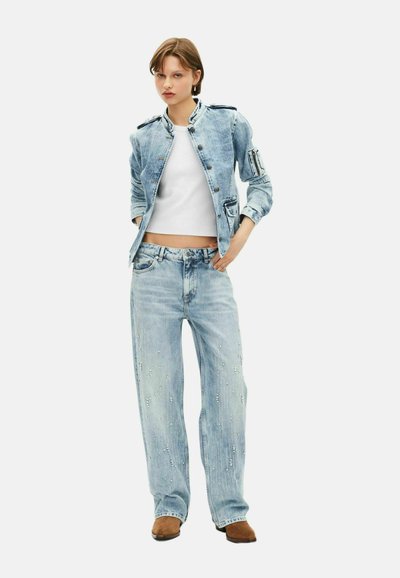 Veste en denim bleu clair avec col montant et fermeture à boutons, associée à un pantalon en denim bleu clair ample avec des détails en perles. Bottes chelsea marron.