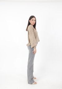 Suéter de punto beige corto con mangas tipo murciélago, combinado con unos vaqueros grises de cintura alta. La modelo se encuentra de perfil, luciendo sandalias de color claro.