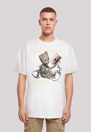 White cotton t-shirt featuring a graphic of a cartoon character holding a cassette tape and black cords, with text "GET YOUR GROOT ON" in yellow.