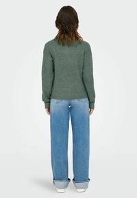 Pull à côtes vert foncé avec un col rond, associé à un jean taille haute bleu clair, à coupe ample et avec des ourlets retroussés.