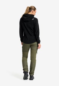 Svart fleece hoodie med en subtil logotyp på axeln, kombinerad med olivgröna cargo-byxor med dragkedjor och fickor. Svarta vandringskängor.