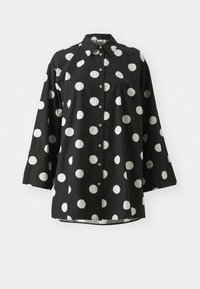 Chemise noire ornée de grands pois blancs, avec un design à boutons, un col et des manches longues aux poignets arrondis.