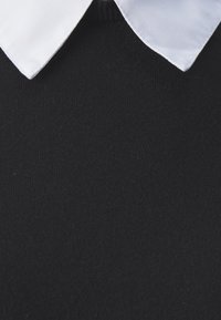 Schwarzer Strickpullover mit weißem Baumwollhemdkragen. Die Oberfläche ist glatt mit einem feinen Strickmuster.