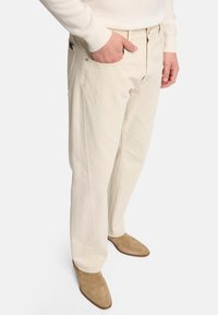 Pantaloni in cotone beige con una vestibilità comoda, dotati di tasche laterali e di una vita classica, abbinati a stivaletti alla caviglia in suede color tan.