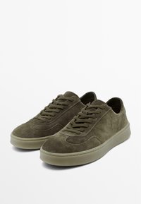 Olijfgroene suède sneakers met een ronde neus, platte rubberen zool en een klassieke vetersluiting met subtiele stiksel details.