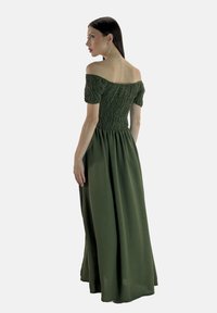 Abito aderente, con spalle scoperte, di colore verde scuro, caratterizzato da una texture smock e una gonna maxi fluida. Tessuto liscio con una leggera lucentezza.