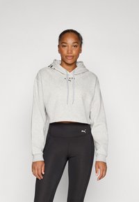 Felpa grigia corta con cappuccio e lacci, abbinata a leggings neri a vita alta con un piccolo logo, texture liscia su tutta la superficie.