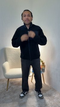 Zwarte fleece jas met ritssluiting en hoge kraag, twee zijzakken, gecombineerd met donkere jeans en zwarte sneakers met witte accenten.