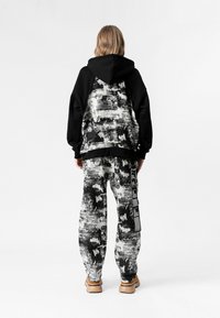 Sudadera negra con capucha y patrón abstracto blanco en la parte posterior, combinada con pantalones jogger negros y blancos con un diseño estampado y detalles de cinta.