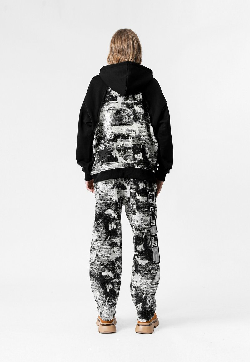 Sudadera negra con capucha y patrón abstracto blanco en la parte posterior, combinada con pantalones jogger negros y blancos con un diseño estampado y detalles de cinta.