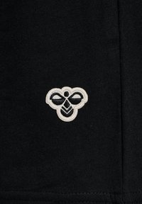 Svart tyg med en texturerad broderad logotyp i vitt, med en stiliserad bi-design med vingar och chevrons i basen.