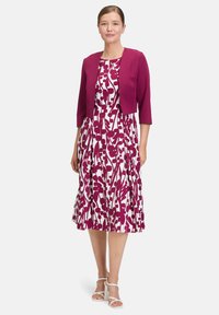 Fuksjowa bolero na białej sukience z magentowymi kwiatowymi wzorami; plisowana spódnica i białe buty na zamkniętej podeszwie dopełniają stylizację.