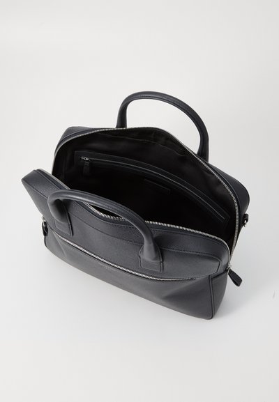 Sacoche pour ordinateur en cuir noir avec poignées supérieures, une poche avant et une fermeture éclair en argent. L'intérieur comprend un compartiment principal et une poche zippée.