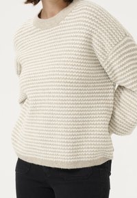 Dzianinowy sweter w kremowym kolorze z teksturowymi poziomymi paskami. Okrągły dekolt, opadające ramiona i miękka tkanina. Połączony z czarnymi spodniami.