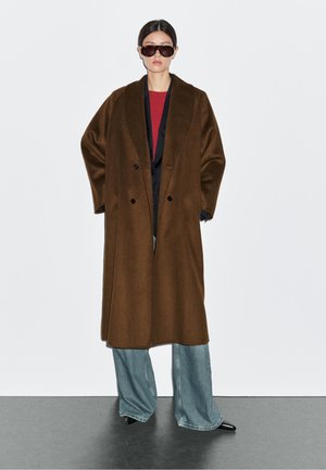 Brown wool coat with a double-breasted design, large lapels, and side pockets, paired with oversized blue jeans and black shoes.