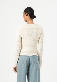Knit long-sleeve sweater in off-white with a textured striped pattern. Features a round neckline and fitted silhouette, paired with light blue jeans.