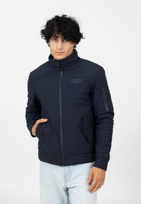 Navyblaue Bomberjacke aus weichem, glattem Material. Mit hohem Kragen, Reißverschluss und seitlichen Taschen. Schmal geschnittenes Design mit Logo-Detail.