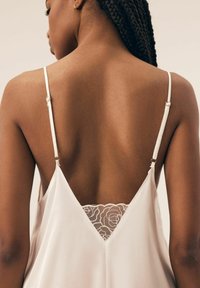 Sukienka satinowa w jasnym kremowym kolorze z cienkimi ramiączkami. Posiada głęboki dekolt w kształcie litery V z delikatnymi koronkowymi detalami o wzorze kwiatowym na górnej części pleców.