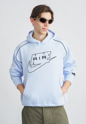 Lichtblauwe hoodie met zwart logo en accenten, voorzien van een kangeroezak en geribbelde manchetten. Gecombineerd met groene cargobroek.