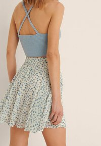 Světlomodrý žebrovaný krátký top s překříženými ramínky v kombinaci s krátkou, vzdušnou sukní s květinovým vzorem v modrých a béžových tónech.