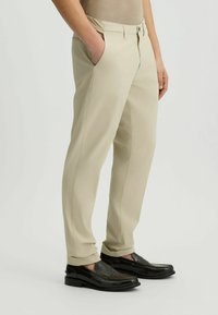 Pantalones beige con corte recto, bolsillos laterales y una textura suave. Combinados con zapatos de cuero oscurecidos sin cordones.