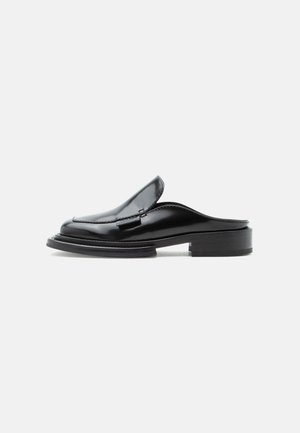 Mustast nahast libisevad madala kogumkontsaga mulesussid, mille ülemisel osal on õmblused, näidatud küljelt ühtlasel taustal.