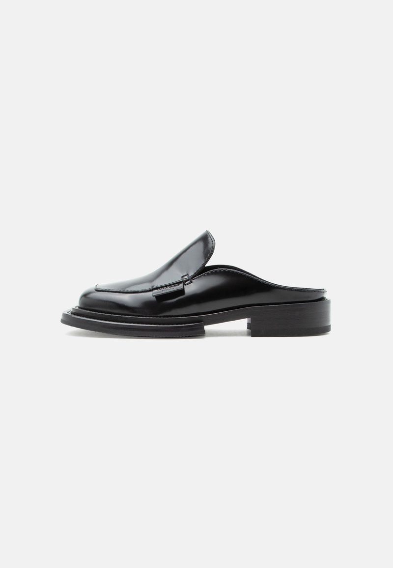 Μαύρο δερμάτινο παπούτσι mule με χαμηλό στημόνι και ραμμένη λεπτομέρεια στο πάνω μέρος, απεικονίζεται από το πλάι σε απλό φόντο.