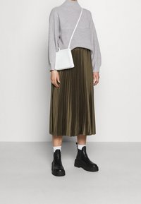 Pull douillet en tricot gris clair, jupe midi plissée olive, sac bandoulière blanc, bottines noires à semelles  épaisses et chaussettes blanches.