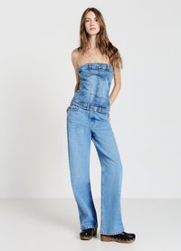 Top senza spalline in denim con bottoni frontali, abbinato a jeans a gamba larga azzurri. L'outfit è completato da sabot neri con suola in legno.