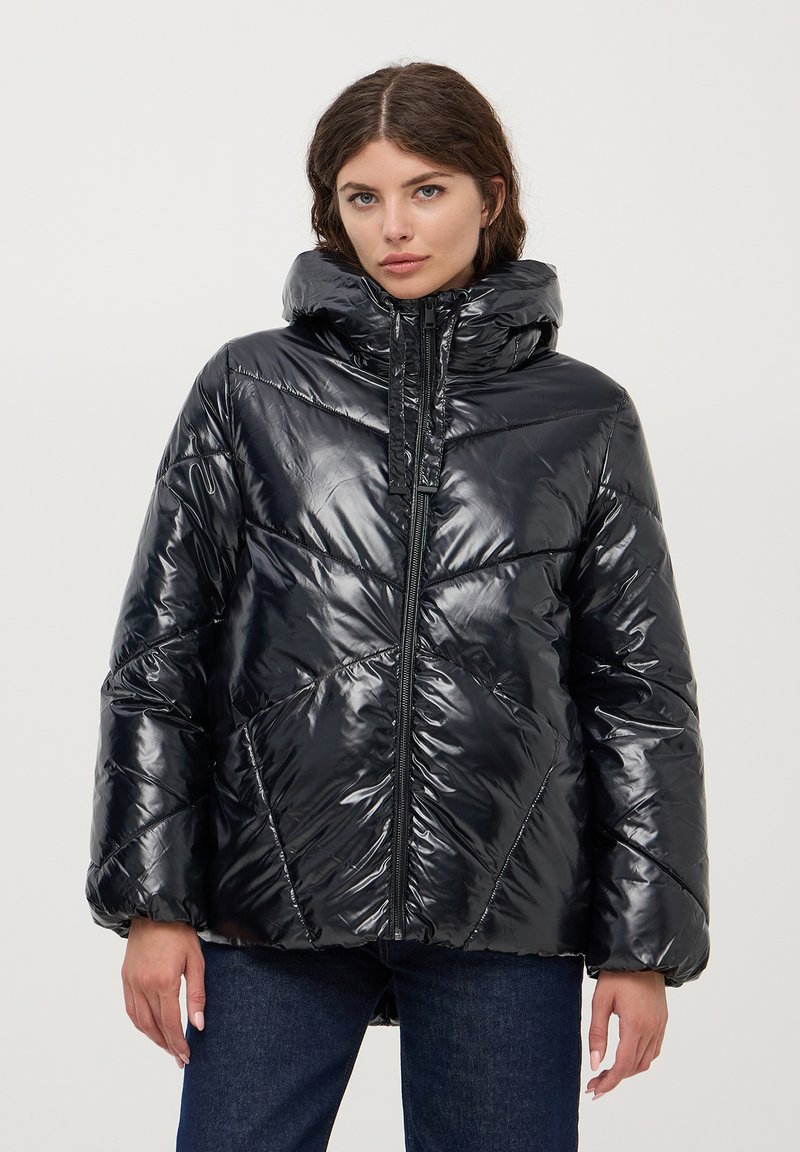 Giubbotto puffer nero con finitura lucida, cappuccio, zip verticale e motivo a rombi. Indossato sopra jeans scuri.