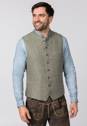 Graue Leinenweste mit Kragen, fünf Knöpfen und einer Fronttasche, über einem hellblauen langärmeligen Hemd getragen. Kombiniert mit braunen bestickten Hosen.