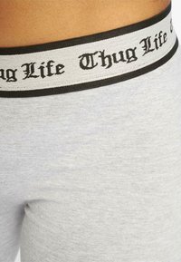 Grijze katoenen shorts met een brede zwart-witte tailleband waarop "Thug Life" in een decoratief lettertype is gedrukt. Zachte textuur, aansluitend ontwerp.
