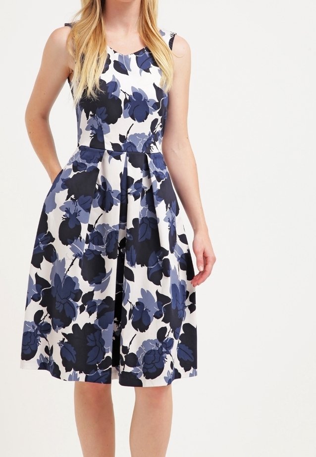 Vestido en línea A con estampado floral sobre una base blanca, con grandes flores azules y negras. Tiene un escote redondo y un diseño sin mangas, con una cintura ajustada.