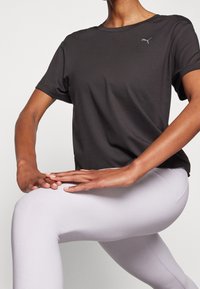 Svart atletisk t-shirt med korta ärmar och rund halsringning med en Puma-logotyp på bröstet, ihop med ljusgråa, åtsittande leggings.