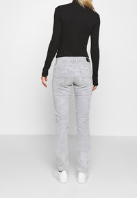 Jasnoszare dżinsy o dopasowanym kroju, z tylnymi kieszeniami ozdobionymi falistymi wzorami i delikatnym rozciągnięciem. Połączone z czarną bluzką z długim rękawem.
