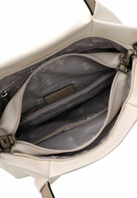 Intérieur d'un sac à main en cuir blanc avec plusieurs compartiments, doublure grise présentant un motif logo subtil, et une poche zippée.