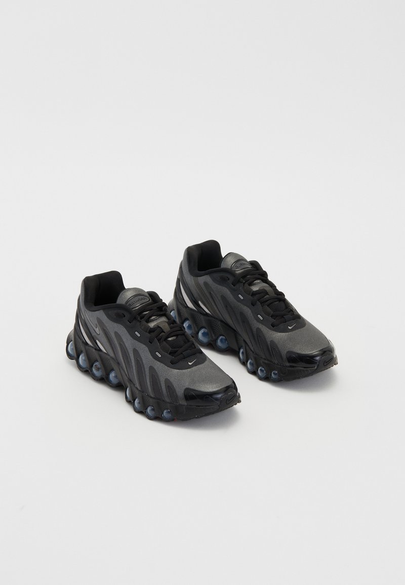 Chaussures de sport noires au design épuré, dotées d'un dessus texturé, d'un système de laçage arrondi et d'accents de semelle distinctifs en forme de bulle.