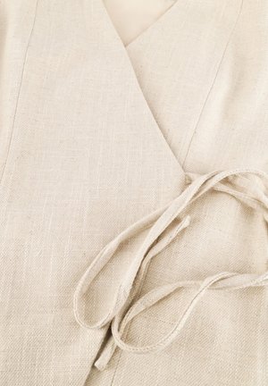 Close-up van beige gestructureerde wikkelstof die vastgebonden is met een bijpassende stoffen riem in een losse knoop.