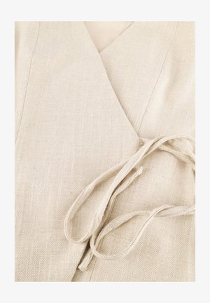 Close-up van beige gestructureerde wikkelstof die vastgebonden is met een bijpassende stoffen riem in een losse knoop.