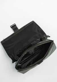 Borsa di tessuto nero con una rifinitura verde, dotata di un interno con zip e diversi scomparti. Chiusura assicurata da una cintura.