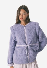 Fioletowa polarowa kurtka z długimi rękawami, teksturowana tkanina, zapi�ęcie na zamek z przodu, dwie kieszenie i ściągacz w talii. Wykończona białymi detalami.