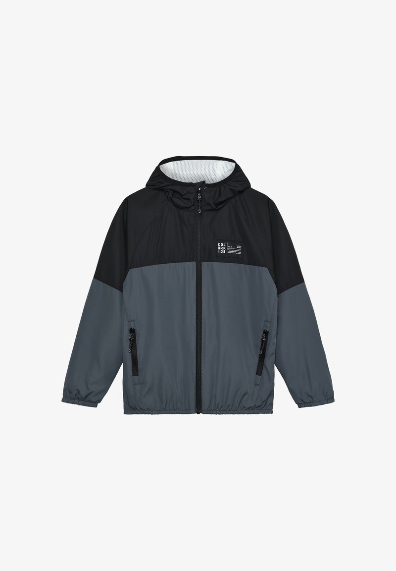 Grå og sort vindjakke med hætte, frontlynlås og to sidelommer med lynlås samt elastiske manchetter. Fremstillet af let, glat materiale.