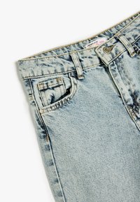 Jeans in denim blu chiaro con vestibilità ampia, dotati di tasca frontale, cuciture a contrasto e chiusura con bottone in metallo alla vita.