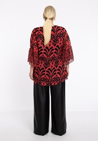Rote Bluse mit schwarzem Blumenmuster, leichtes Material, geraffte lange Ärmel, kombiniert mit locker sitzenden schwarzen Kunstlederhosen.