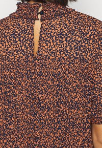 Marineblå topp med orange leopardtryck, med en rutig krage och en liten nyckelhålsöppning bak, texturerat tyg med veck.