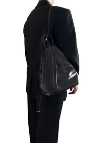 Černý kožený batoh se štíhlým designem, obsahující přední kapsu a nastavitelné popruhy. Texturovaný povrch s jemným leskem.