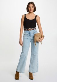 Black tank top with decorative straps, light blue wide-leg jeans, leopard print belt, tan suede ankle boots, and beige fringed handbag.