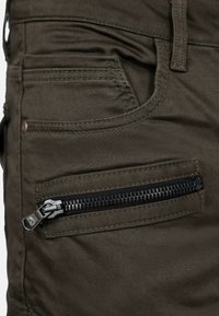 Olivgrüne Hose aus robustem Stoff, mit einer Vordertasche und einer seitlichen Tasche mit Reißverschluss und schwarzem Reißverschlussbeschlag.