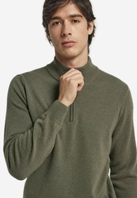 Oliwkowo-zielony pulower z wysokim kołnierzem i półzamkiem. Wykonany z miękkiej, teksturowanej tkaniny, z prążkowanymi mankietami i ściągaczem.