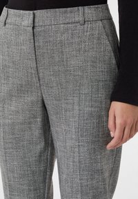 Grijs gestreepte broek met een gestructureerde stof, met een platte voorkant en zijzakken. Close-up opname toont een hand die op de stof rust.
